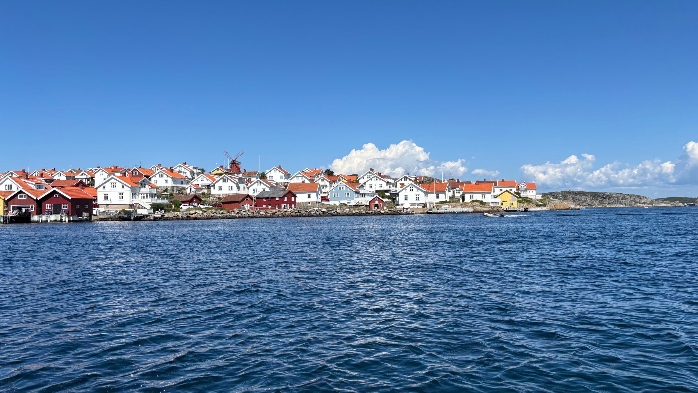 Mollösund från vattnet, med kvarnen över vita hus, röda tak och sjöbodar